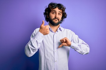 Young handsome business man with beard wearing shirt standing over purple background Doing thumbs up and down, disagreement and agreement expression. Crazy conflict