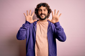 Young handsome sporty man with beard wearing casual sweatshirt over pink background showing and pointing up with fingers number ten while smiling confident and happy.