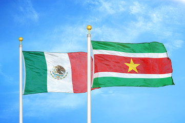Mexico and Suriname two flags on flagpoles and blue cloudy sky