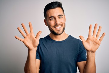 Young handsome man wearing casual t-shirt standing over isolated white background showing and pointing up with fingers number ten while smiling confident and happy.