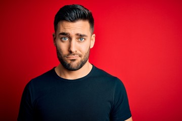 Young handsome man wearing casual black t-shirt standing over isolated red background depressed and worry for distress, crying angry and afraid. Sad expression.