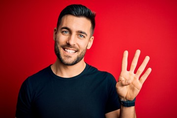 Naklejka premium Young handsome man wearing casual black t-shirt standing over isolated red background showing and pointing up with fingers number four while smiling confident and happy.