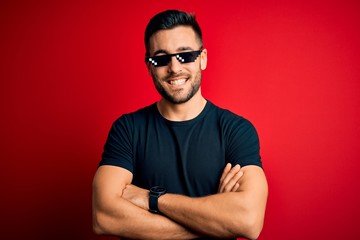 Young handsome man wearing funny thug life sunglasses over isolated red background happy face...