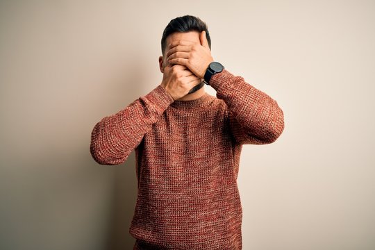 Young handsome man wearing casual sweater standing over isolated white background Covering eyes and mouth with hands, surprised and shocked. Hiding emotion