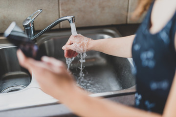 flattening the curve through hygiene against covid-19, woman washing her hands while scrolling social media or news on her smartphone