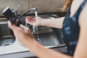 flattening the curve through hygiene against covid-19, woman washing her hands while scrolling social media or news on her smartphone