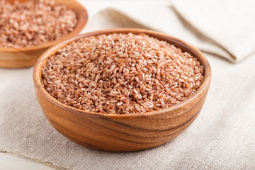 Two wooden bowls with unpolished brown rice on a white wooden background. Side view, close up.