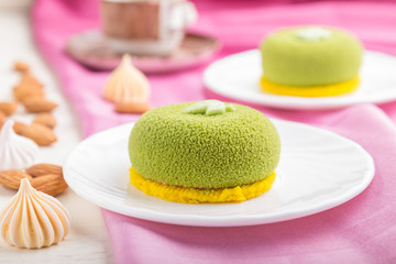 Green mousse cake with pistachio cream and a cup of coffee on a pink textile background. side view, selective focus.