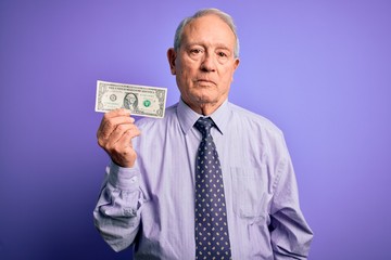 Senior grey haired man holding one dollar bank note over purple background with a confident expression on smart face thinking serious