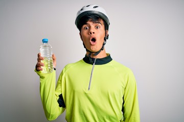 Young handsome cyclist man wearing security bike helmet drinking bottle of water scared in shock with a surprise face, afraid and excited with fear expression