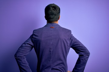 Young handsome business man wearing jacket and glasses over isolated purple background standing backwards looking away with arms on body