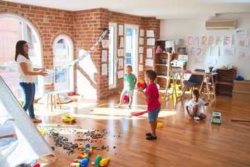 Young beautiful teacher and toddlers playing basketball around lots of toys at kindergarten