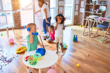 Young beautiful teacher and toddlers playing around lots of toys at kindergarten