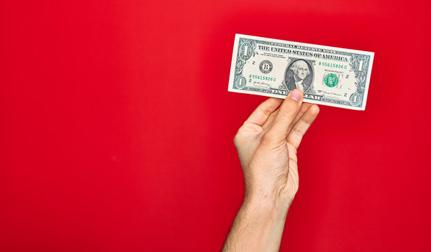 Beautiful hand of man holding one dollar banknote over isolated red background
