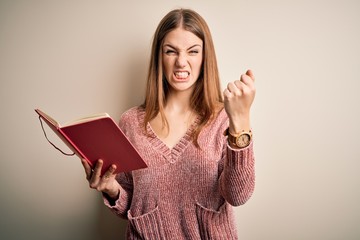 Young beautiful redhead student woman reading book over isolatated white background annoyed and frustrated shouting with anger, crazy and yelling with raised hand, anger concept