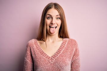 Fototapeta premium Young beautiful redhead woman wearing casual sweater over isolated pink background sticking tongue out happy with funny expression. Emotion concept.