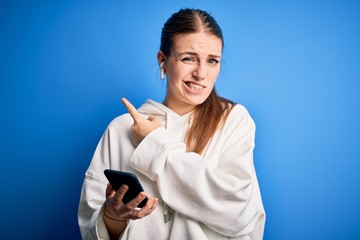 Young redhead sportswoman doing sport listening to music using earphones and smartphone Pointing aside worried and nervous with forefinger, concerned and surprised expression