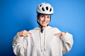 Young beautiful redhead cyclist woman wearing bike helmet over isolated blue background looking confident with smile on face, pointing oneself with fingers proud and happy.