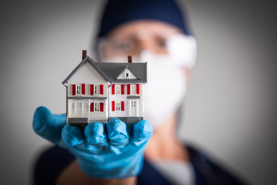 Female Doctor or Nurse Wearing Surgical Gloves Holding Model Home