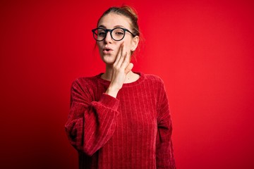 Young beautiful redhead woman wearing casual sweater over isolated red background hand on mouth telling secret rumor, whispering malicious talk conversation