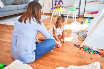 Caucasian girl kid playing and learning at playschool with female teacher. Mother and daughter at playroom around toys playing with bulding blocks