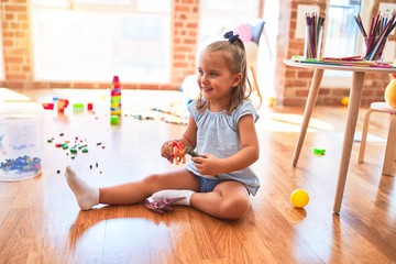 Young beautiful blonde girl kid enjoying play school with toys at kindergarten, smiling happy...