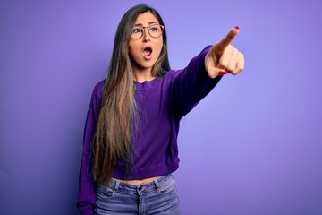 Young beautiful smart woman wearing glasses over purple isolated background Pointing with finger surprised ahead, open mouth amazed expression, something on the front