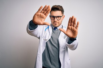 Young doctor man with blue eyes wearing medical coat and stethoscope over isolated background doing frame using hands palms and fingers, camera perspective