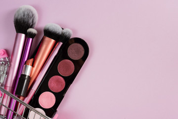 Obraz na płótnie Canvas Eye shadow blush, lipstick and various makeup brushes in a pink trolley of the buyer. The concept of online shopping decorative cosmetics, discounts in stores