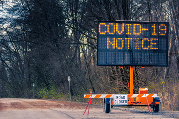Large electronic notification sign on rural street announcing road closure due to Coronavirus...