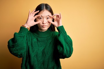 Young beautiful asian woman wearing green winter sweater over yellow isolated background Trying to open eyes with fingers, sleepy and tired for morning fatigue