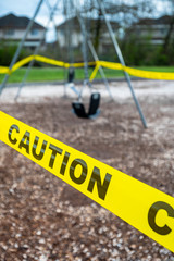 Black rubber swings in closed public playground surrounded by yellow caution tape during Corvid-19 Coronavirus pandemic