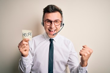 Young call center operator man wearing headset holding paper note with help word screaming proud and celebrating victory and success very excited, cheering emotion