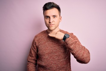 Young handsome caucasian man wearing casual winter sweater over pink isolated background cutting throat with hand as knife, threaten aggression with furious violence