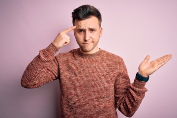Fototapeta premium Young handsome caucasian man wearing casual winter sweater over pink isolated background confused and annoyed with open palm showing copy space and pointing finger to forehead. Think about it.