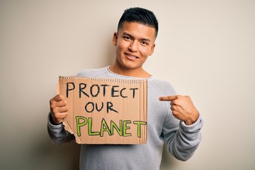 Young handsome activist latin man holding banner asking to protect our planet with surprise face...