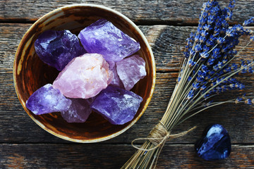 A table top image of a pottery bowl with large rose quartz and amethyst crystal with dried lavender...