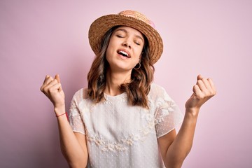 Young beautiful blonde girl wearing summer hat over pink isolated background very happy and excited doing winner gesture with arms raised, smiling and screaming for success. Celebration concept.