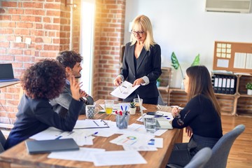 Group of business workers smiling happy and confident. Working together with smile on face. Middle age beautiful woman standing explaining documents at the office