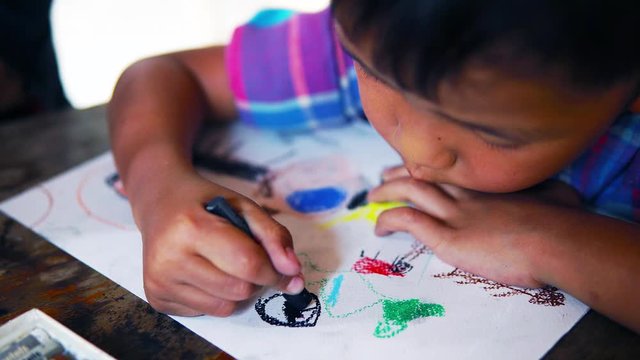 Close up of the Asian boy drawing on paper with color pastel pencil. 
