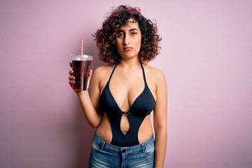 Beautiful arab woman on vacation wearing swimsuit drinking cola refreshment using straw with a confident expression on smart face thinking serious