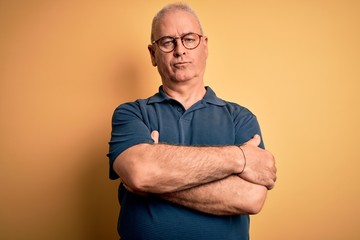 Middle age handsome hoary man wearing casual polo and glasses over yellow background skeptic and nervous, disapproving expression on face with crossed arms. Negative person. - obrazy, fototapety, plakaty