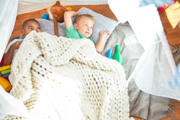 Adorable toddlers playing inside tipi around lots of toys at kindergarten