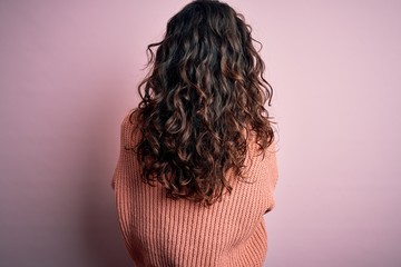 Young beautiful woman with curly hair wearing casual sweater over isolated pink background standing backwards looking away with crossed arms