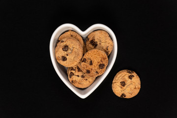 Chocolate chip cookies in a heart shaped bowl on a black background.