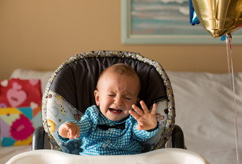 One year old cute boy crying. First Happy birthday. Boy wearing celebration shirt, sitting on a highchair