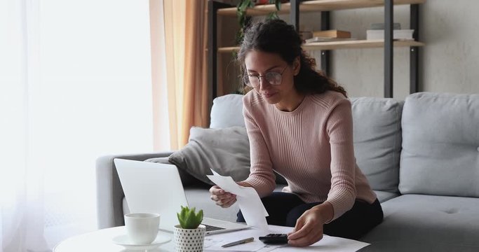 Young woman holding paper bills or paychecks calculating money expenses, tax refund, planning budget at home. Female housewife using laptop and calculator for financial accounting internet payments.