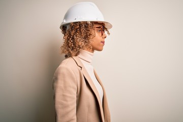 Young african american curly architect woman wearing safety helmet and glasses looking to side,...