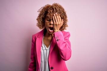 Young african american businesswoman wearing glasses standing over pink background Yawning tired covering half face, eye and mouth with hand. Face hurts in pain.