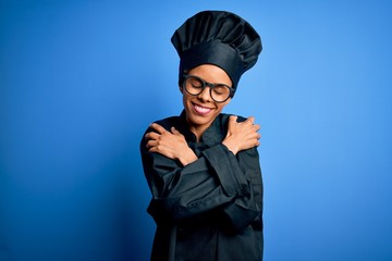 Young african american chef woman wearing cooker uniform and hat over blue background Hugging oneself happy and positive, smiling confident. Self love and self care